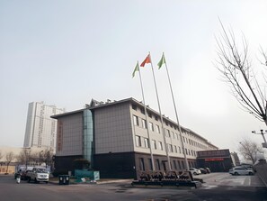 A modern building with a large sign, multiple flags, and parked cars. - Greentree Eastern Hotel Binzhou Zhonghai International Convention and Exhibition Center (Binzhou)