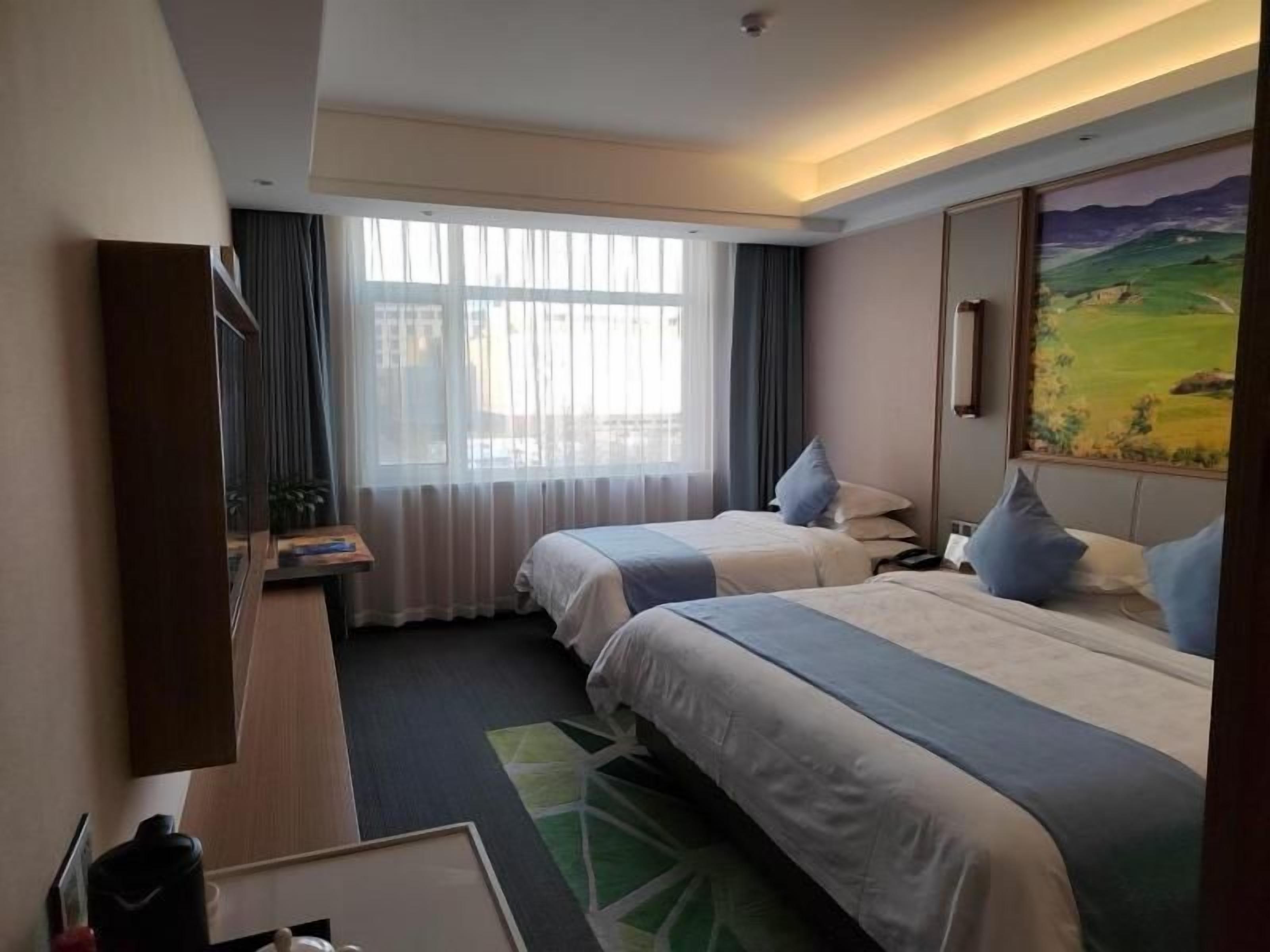 Habitació d'hotel amb dos llits, escriptori, cadira, finestra amb cortines i un quadre a la paret.