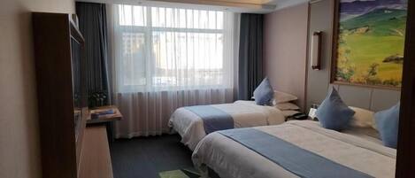 Habitació d'hotel amb dos llits, escriptori, cadira, finestra amb cortines i un quadre a la paret.