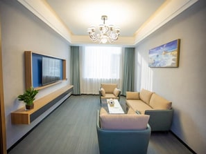 Una camera d'albergo moderna con TV a schermo piatto, divano, tavolino da caffè e un quadro appeso al muro.