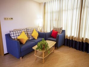 A living room with a blue sofa set, yellow and red cushions, a wooden coffee table with a plant, and a view of a window with curtains. - Greentree Eastern Hotel Binzhou Zhonghai International Convention and Exhibition Center (Binzhou)
