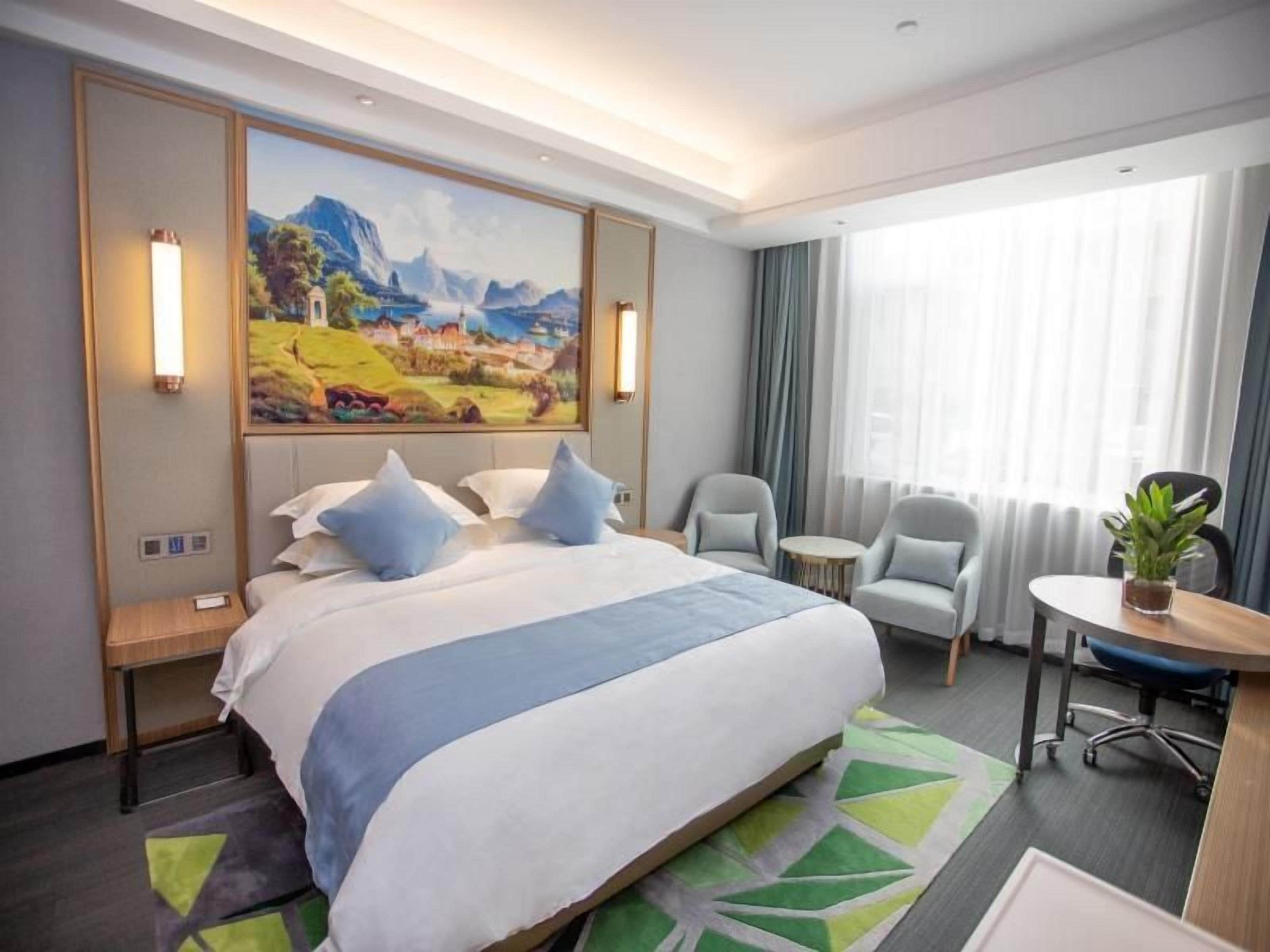 A hotel room with a large bed, two armchairs, a small table, and a painting on the wall.