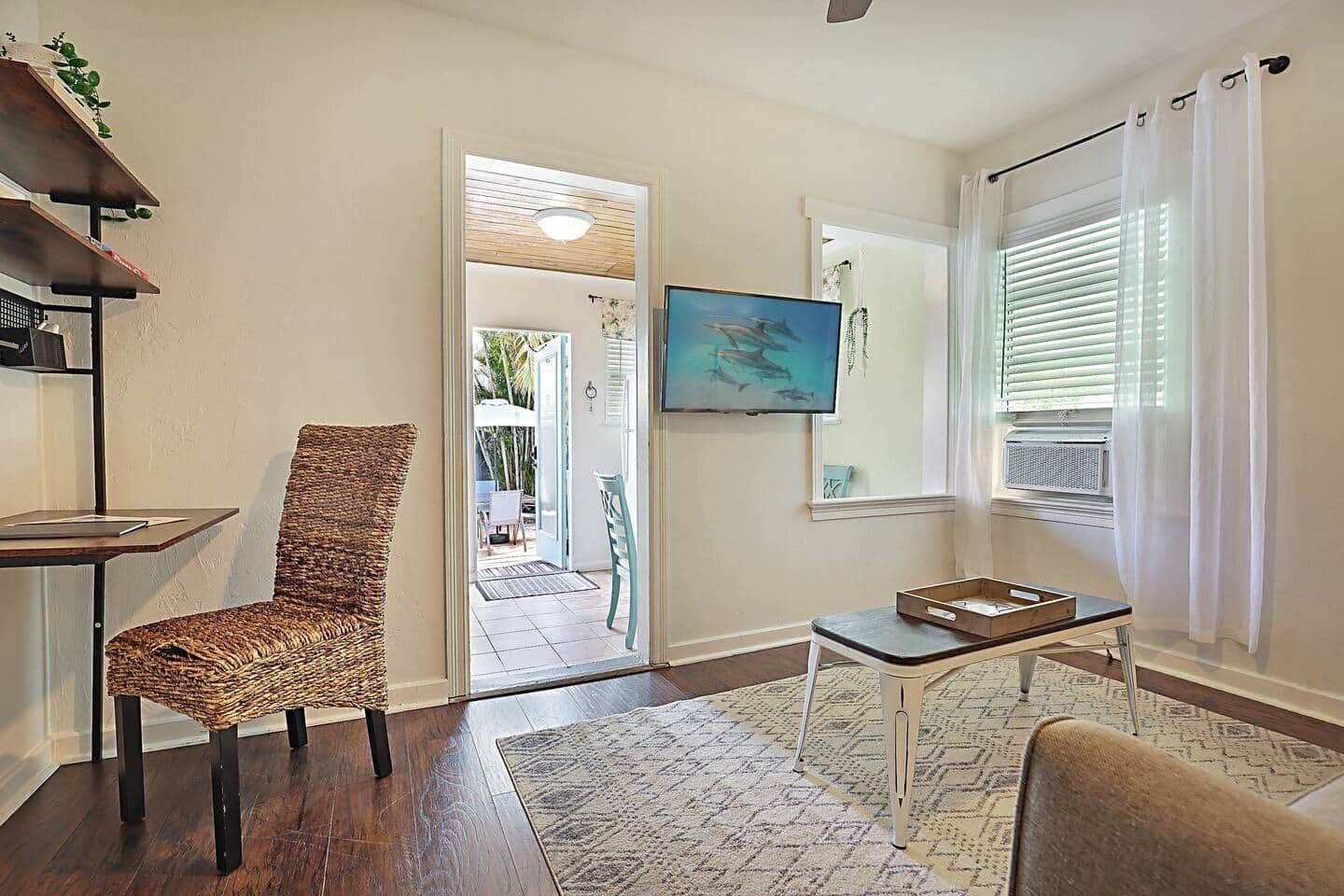 A living room with a wicker chair, a small table, a TV, and a view of the outside.