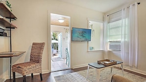 A living room with a wicker chair, a small table, a TV, and a view of the outside. - Steps to Beach & Downtown! Private Patio & Parking (Lake Worth)
