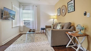 A living room with a ceiling fan, a sofa, a coffee table, a lamp, and artwork on the walls. - Steps to Beach & Downtown! Private Patio & Parking (Lake Worth)
