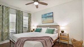 A bedroom with a bed, a ceiling fan, a painting of a beach, and a wicker basket. - Steps to Beach & Downtown! Private Patio & Parking (Lake Worth)