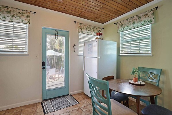 Una cocina con una puerta azul, un refrigerador blanco y una mesa de comedor con sillas.