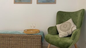 Una habitación con un sillón verde, dos cuadros enmarcados de aves, una mesita de mimbre con dos vasos y una bandeja.