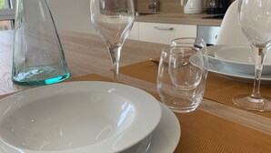 Una mesa de comedor preparada con platos blancos, vasos transparentes, una jofaina de vidrio y cubiertos.