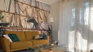 Una sala de estar con un sofá, una mesa de centro de vidrio y un mural en la pared que muestra aparejos de barco.
