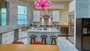Een moderne keuken met een centraal eiland, roestvrijstalen apparatuur en een roze kroonluchter.