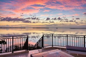 A balcony with a metal railing overlooking a calm body of water and a sunset sky. - Oceanfront Luxe House w/ Rooftop & Private Beach (Key Largo)