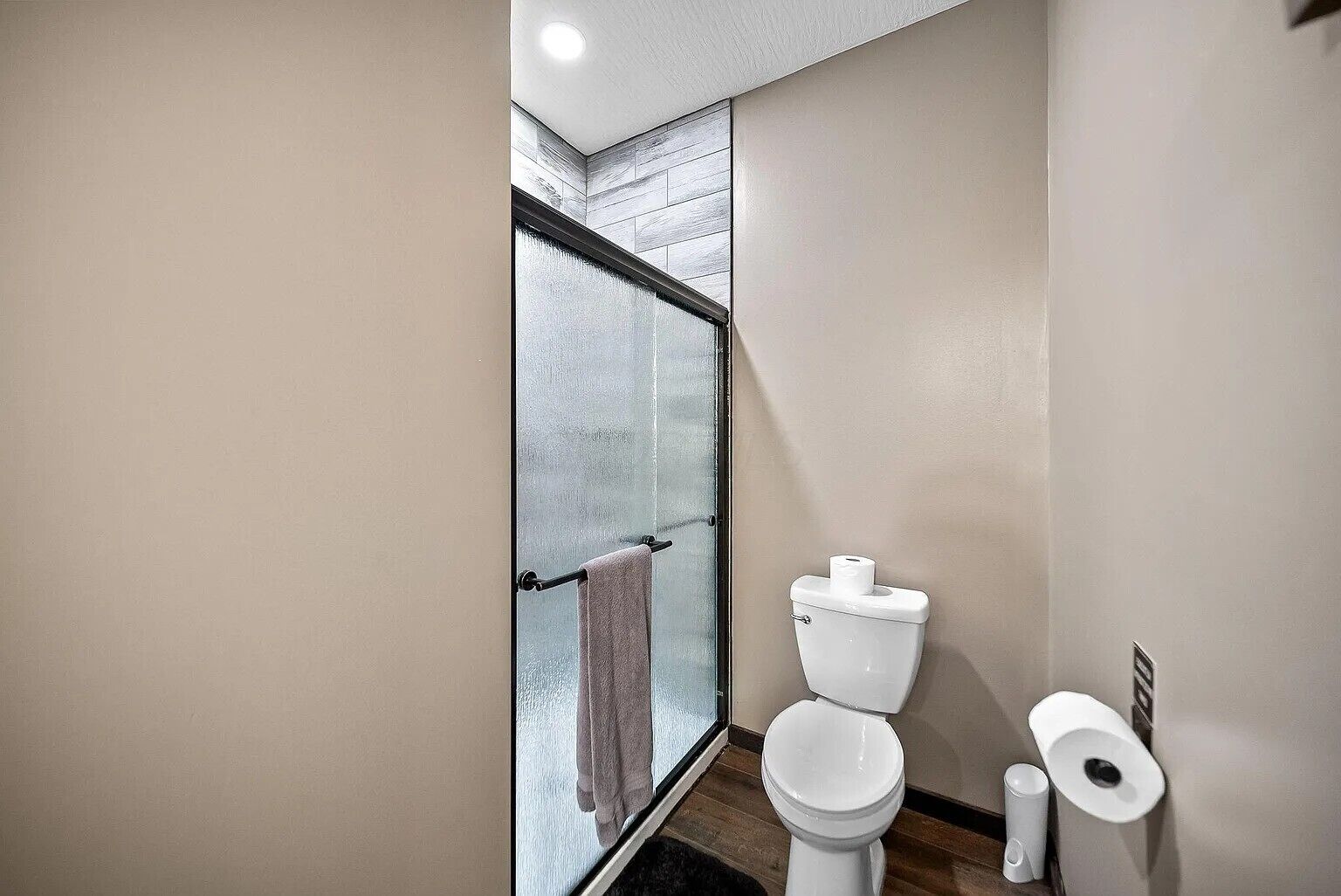 A modern bathroom with a glass shower enclosure, a toilet, and a toilet paper holder.