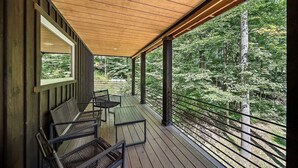 A covered outdoor deck with wooden flooring and metal railings, featuring a table and chairs.