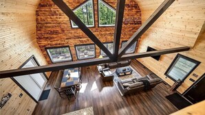 A spacious loft-style room with a high ceiling, wooden walls, and large windows.