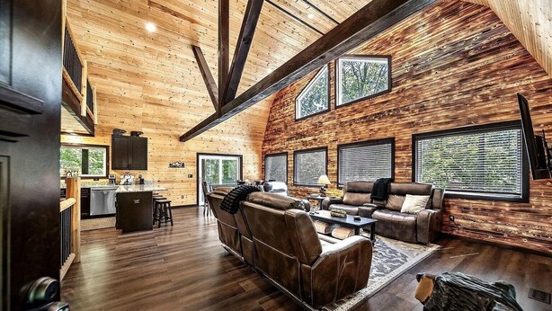 A spacious living area with a high ceiling, wooden walls, and large windows.