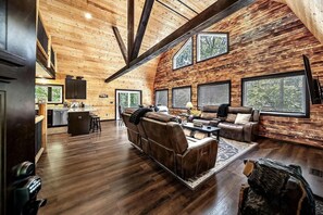 Amplia sala de estar con techo alto, paredes de madera y ventanas grandes.