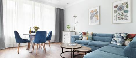 A modern living room with a blue sofa, round coffee table, and a dining area with blue chairs.