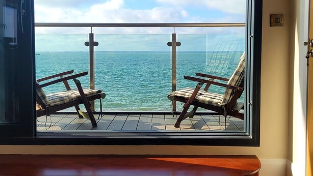 Una stanza con una grande finestra vista su un corpo d'acqua e un balcone con due sedie.