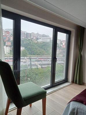 A room with a large window, a green chair, and a bed. - KURT OTEL (Trabzon)