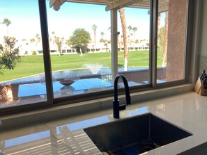 Une cuisine équipée d’un évier, avec une fenêtre donnant sur une piscine et un terrain de golf.