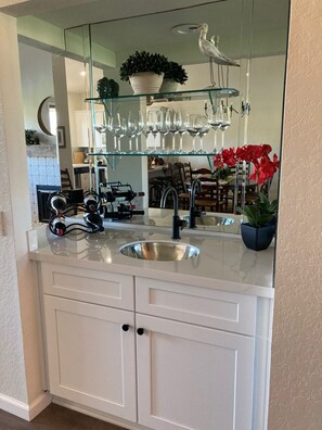 A kitchen with a large mirror, wine glasses, and a potted plant.