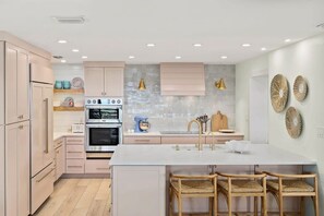 A modern kitchen with a central island, built-in oven, and a large window.