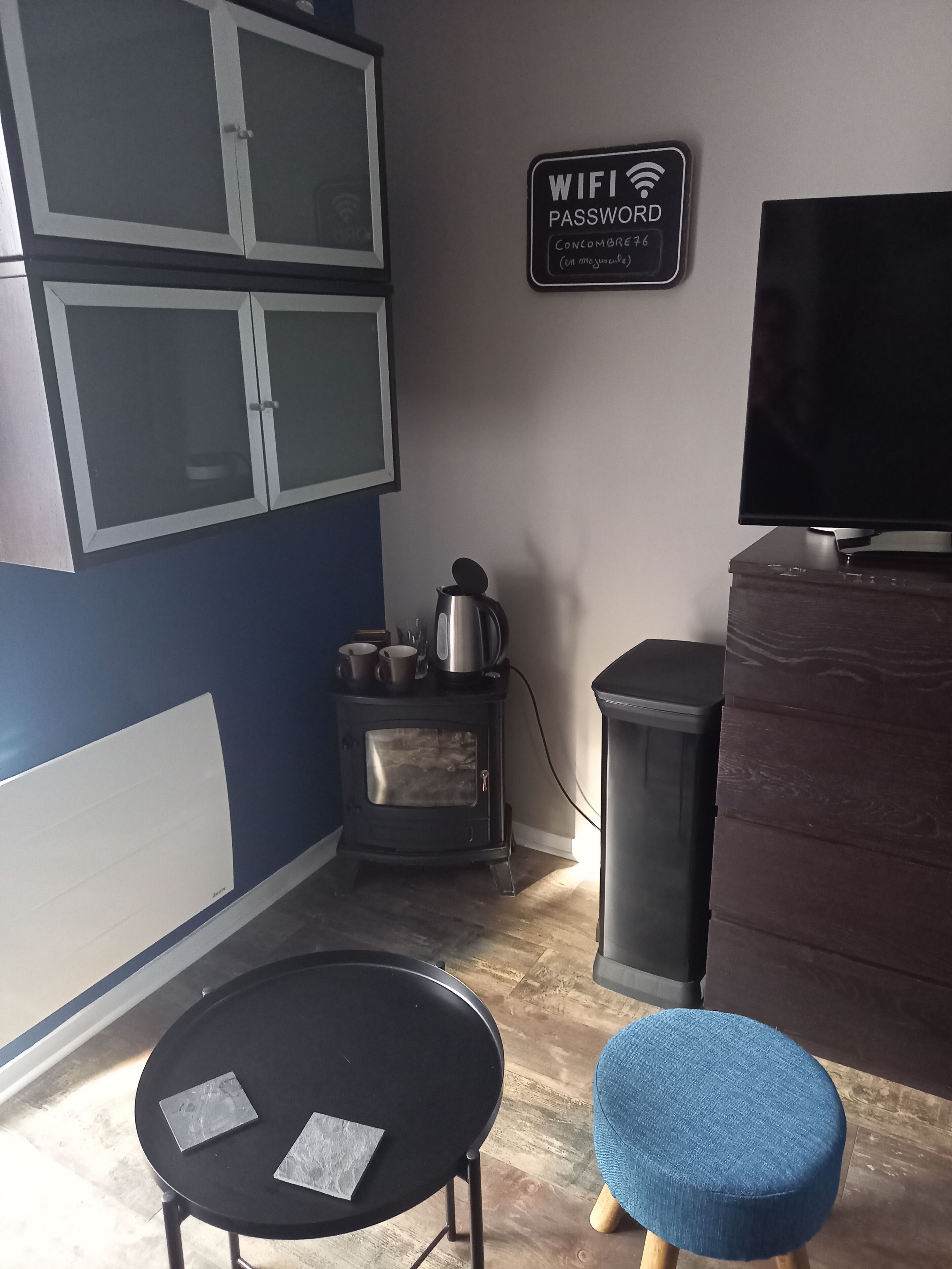 Een knus woongedeelte met kitchenette, een eethoek met een tafeltje en twee krukken, een televisie, en een bord met de WiFi-wachtwoord.