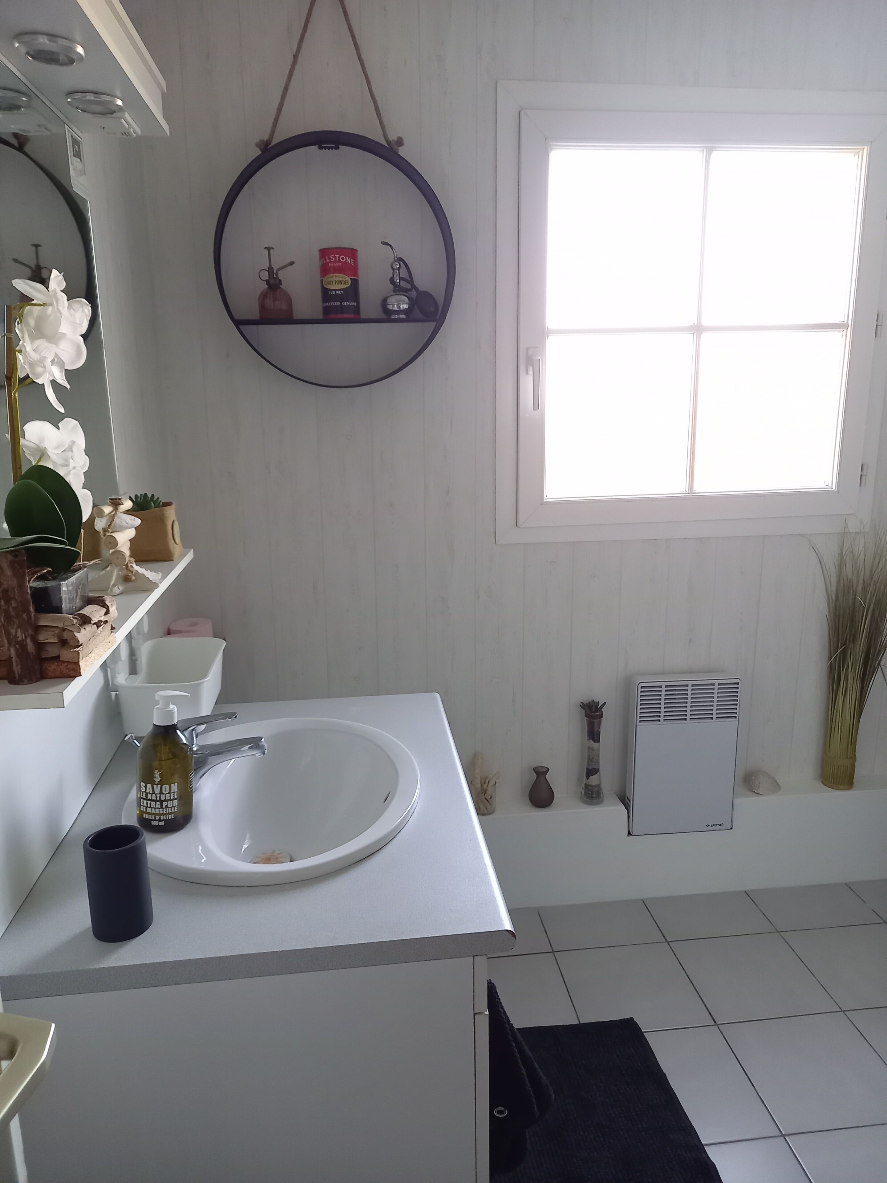 Une salle de bain avec un lavabo blanc, un miroir, une fenêtre et un radiateur.