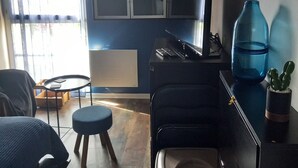 Una sala de estar con una pared azul, un sofá negro, una mesita redonda y un florero azul con un cactus.