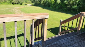 A wooden deck with a view of a grassy field and trees. - Northwoods Cabin near Upper Red Lake (Kelliher)