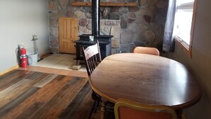 A cozy room with a stone wall, a wooden ceiling, a fireplace, a dining table, and a fire extinguisher. - Northwoods Cabin near Upper Red Lake (Kelliher)