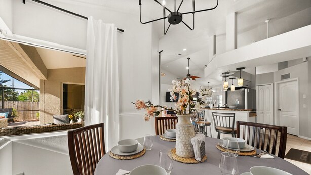 Een eethoek met een ronde tafel voor vier personen, omringd door stoelen. Op de tafel staat een vaas met bloemen, en er is een keuken te zien op de achtergrond.