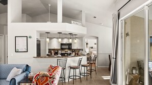 Een moderne keuken met een centraal eiland, barstoelen en een zithoek met een blauwe bank en een decoratief plaid.