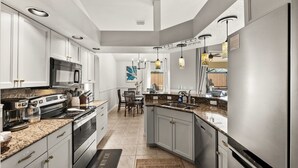 A modern kitchen with granite countertops, stainless steel appliances, and a dining area with a table and chairs. - Beach Time Villa-heated pool & spa-4 bikes, game room-near beach (Venice)