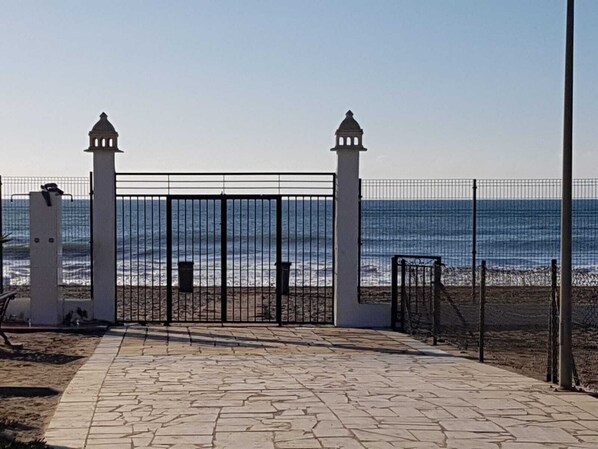 A paved walkway leading to a gated entrance with a view of the sea.