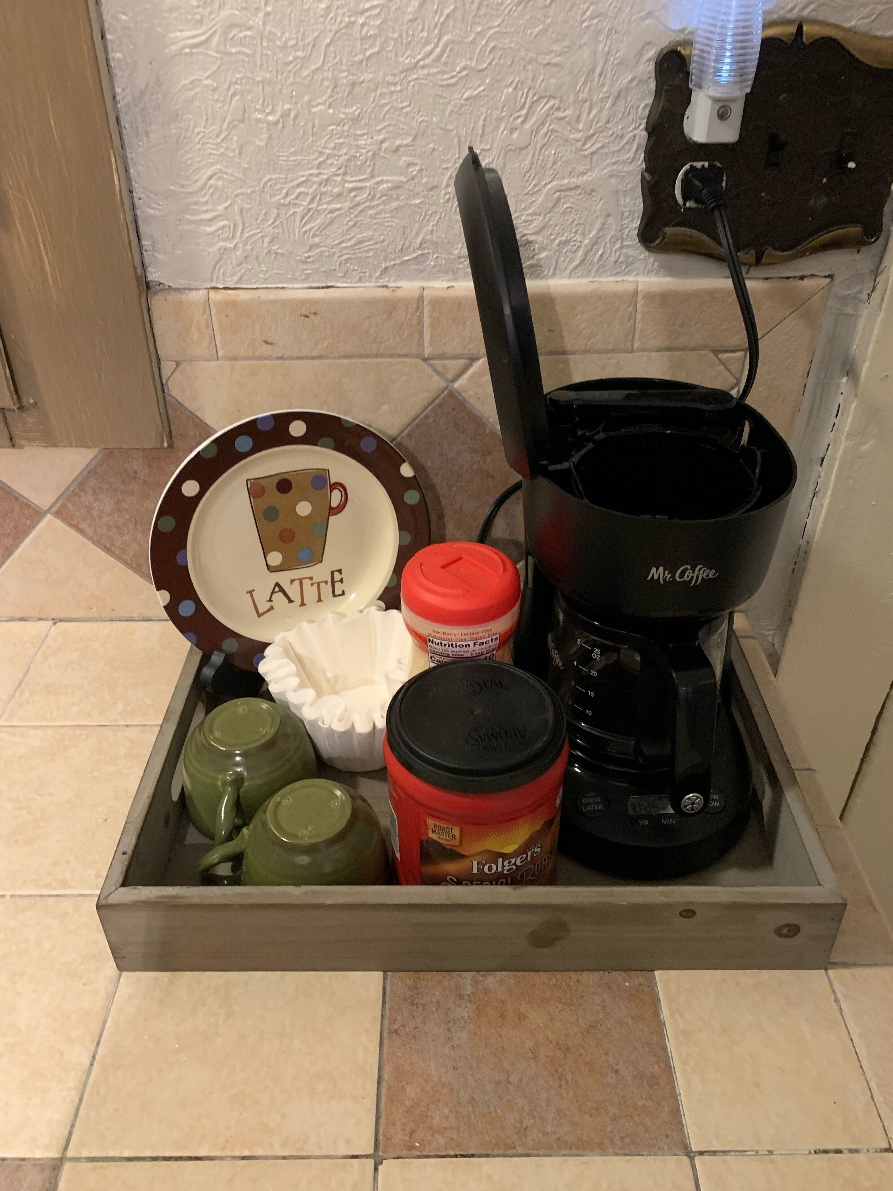 A kitchen drawer containing a coffee maker, a red container, a green teapot, a white cup, and a polka-dotted plate with the word "LATTE".