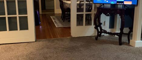 A living room with a TV on a stand, a dining area with a table and chairs, and a hallway leading to another room.