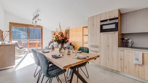 A modern kitchen with wooden cabinets, a dining table set for four, and a large window overlooking a balcony.