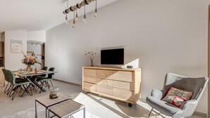 A modern living room with a wooden cabinet, a grey armchair, and a dining area with a table and chairs.