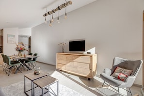 A modern living room with a wooden cabinet, a grey armchair, and a dining area with a table and chairs.
