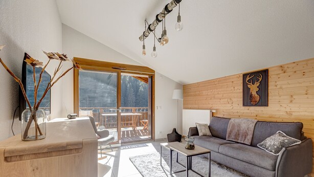 A modern living room with a grey sofa, wooden accents, a glass coffee table, and a view of a balcony with outdoor furniture.