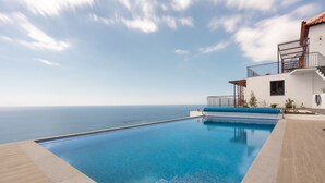 A swimming pool with a view of the sea, a white building with a balcony, and a clear sky. - Apartment Duplex T1 - Duplex WEST (Arco da Calheta)