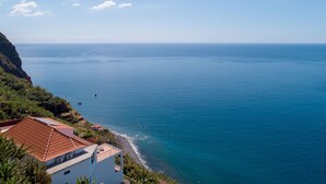 A coastal view with a building featuring a red-tiled roof, a balcony, and a view of the sea. - Apartment Duplex T1 - Duplex WEST (Arco da Calheta)