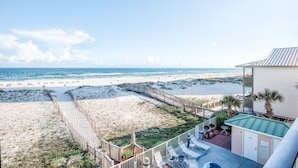 A beach view from a balcony with a wooden deck, a pool area, and a building with a green roof. - Direct Beach Front! You gotta see this view! (Gulf Shores)