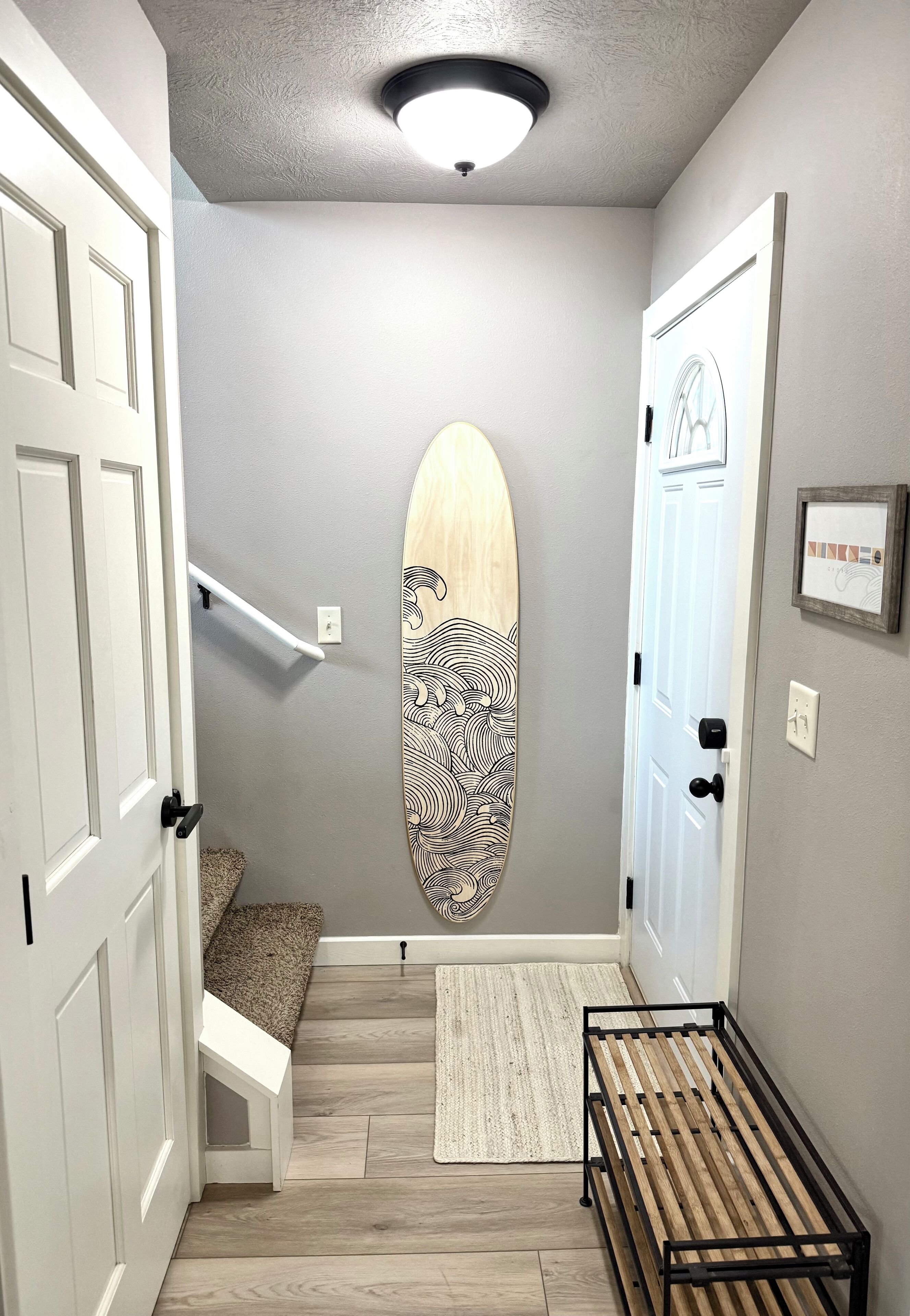 Un couloir avec un banc en bois, une planche de surf accrochée au mur et un petit tapis.