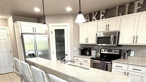 Une cuisine moderne avec des meubles blancs, un grand îlot central doté de tabourets, des appareils en acier inoxydable et un éclairage suspendu.