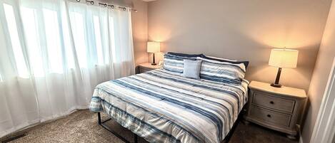 A bedroom with a bed, two bedside tables with lamps, a ceiling fan, and a window with curtains.