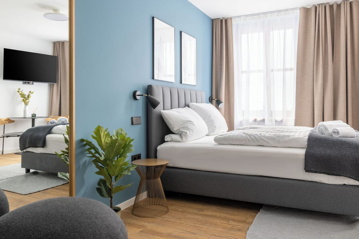 Ein modernes Hotelzimmer mit einem Bett, einem Nachttisch, einer Pflanze und einem Fernseher.