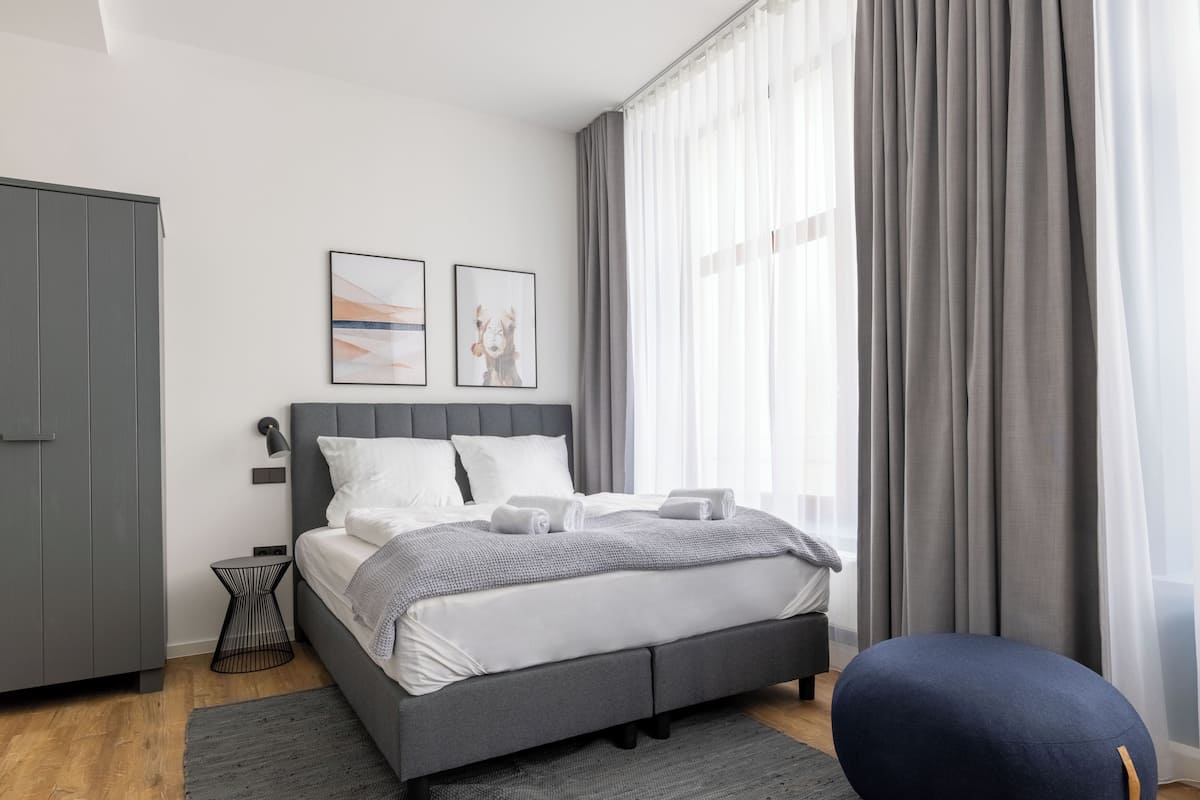 Ein modernes Schlafzimmer mit einem grauen Bett, einem grauen Kleiderschrank und einem runden Pouf.